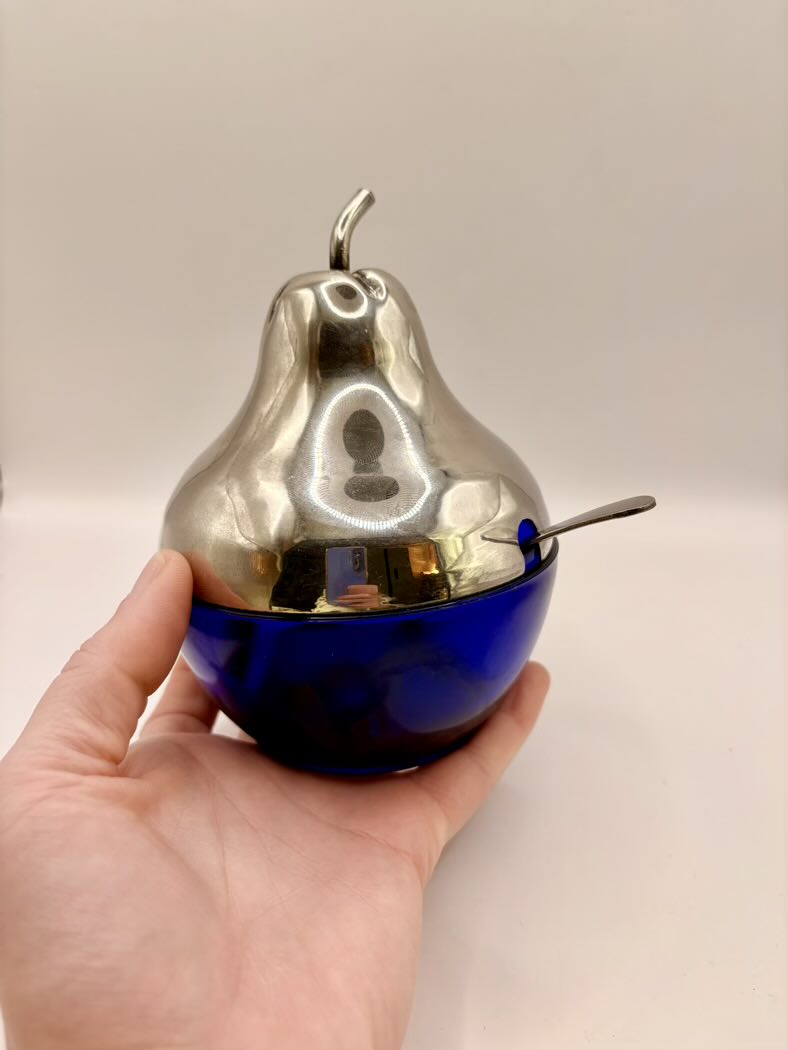 Metallic pear-shaped object with a blue base held in a hand against a plain background