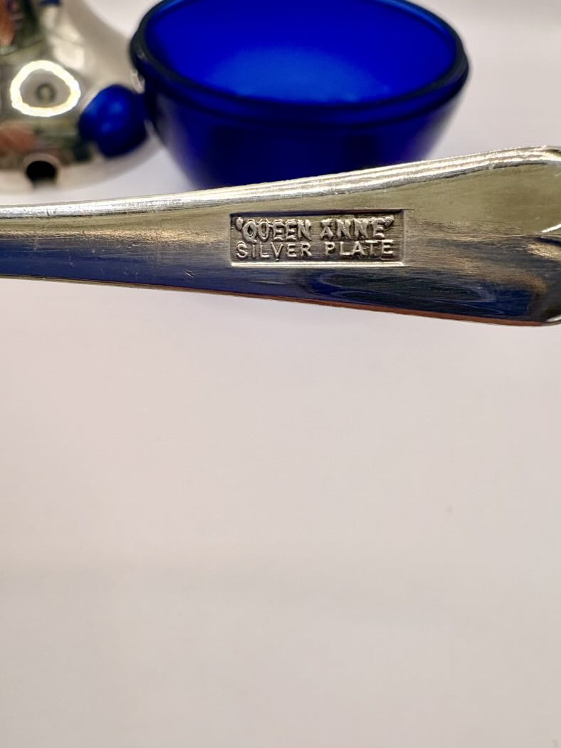 Metallic object with 'Queen Anne Silver Plate' engraving on a white background