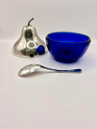 Silver pear-shaped object, blue bowl, and silver spoon on a white background