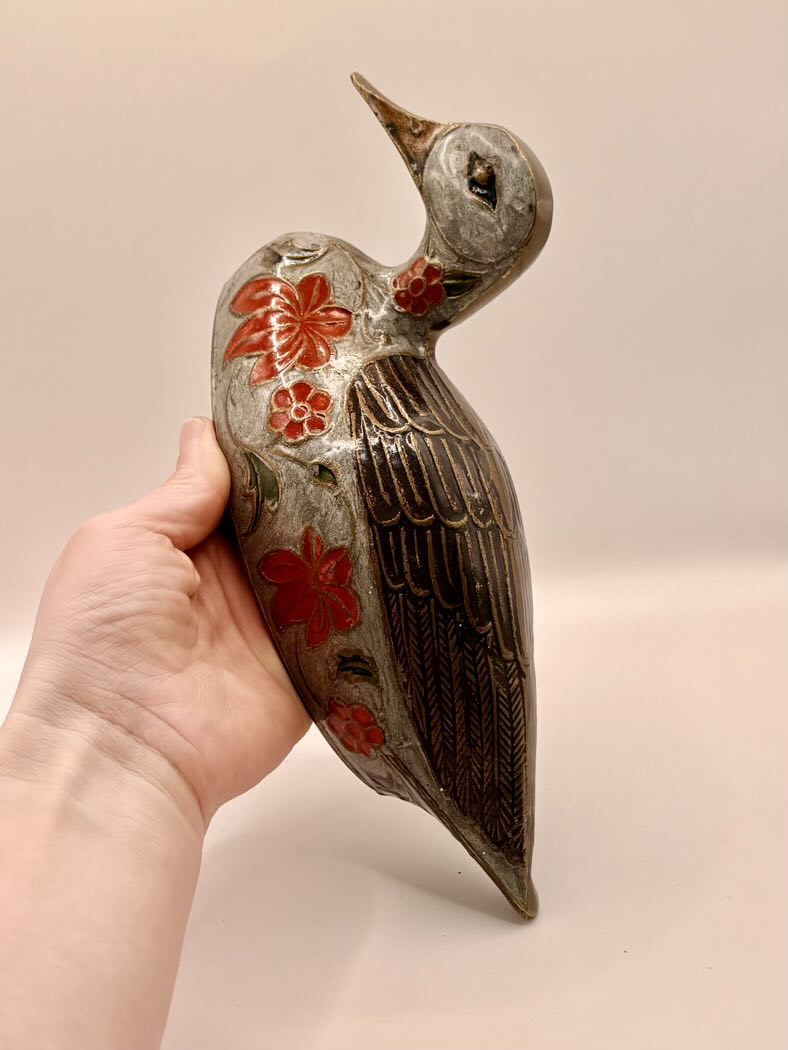Decorative bird figurine with floral patterns held by a hand against a plain background