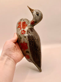 Decorative bird figurine with floral patterns held by a hand against a plain background