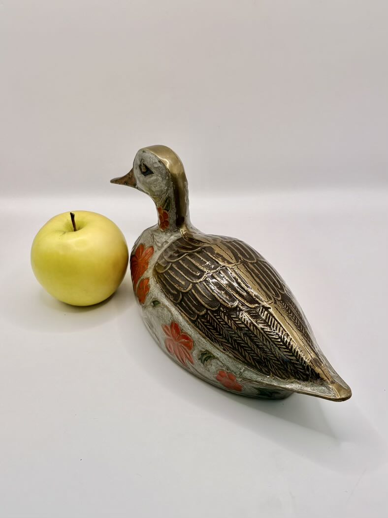 Decorative duck figurine next to a yellow apple on a white background