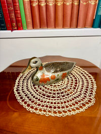 Decorative ceramic duck on a lace doily with books in the background
