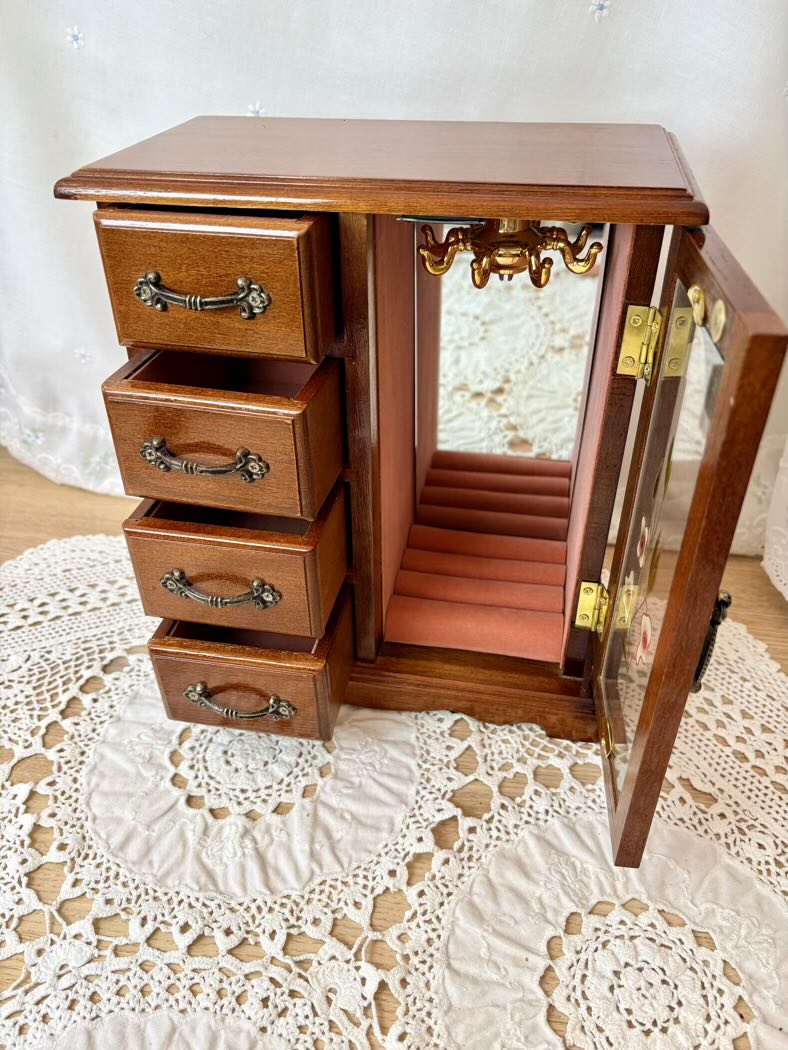 Wooden jewelry cabinet with open door on a lace tablecloth