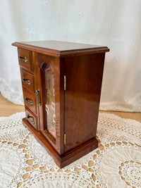 Wooden jewelry cabinet with glass front on a lace tablecloth