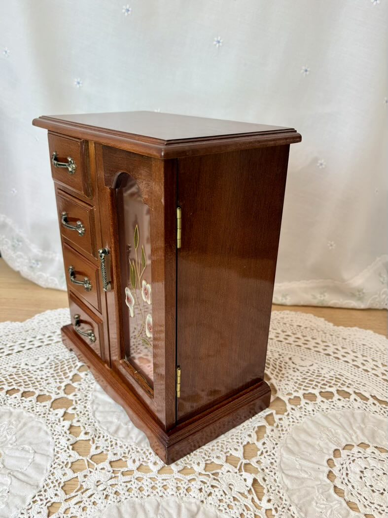 Wooden jewelry cabinet with glass front on a lace tablecloth