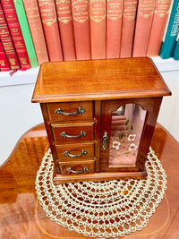 Wooden jewelry box with glass door on a table with books in the background