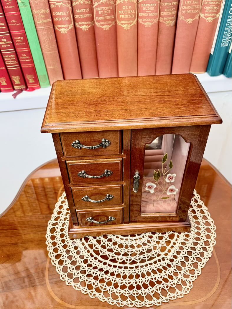 Wooden jewelry box with glass door on a table with books in the background