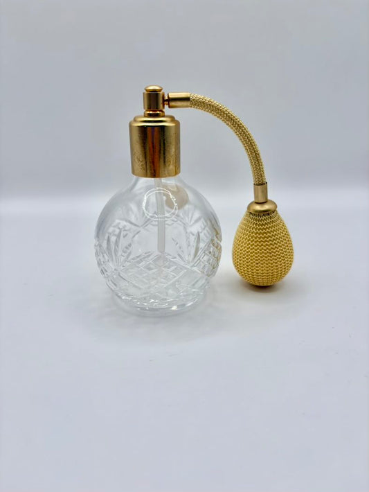 Clear glass perfume bottle with gold cap and spray nozzle on a light gray background