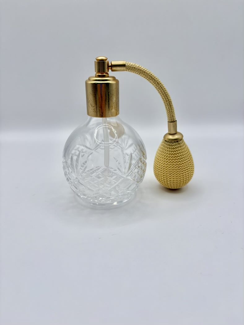 Clear glass perfume bottle with gold cap and spray nozzle on a light gray background