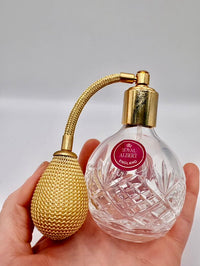 Perfume bottle with gold cap and Royal Albert England label held in hand against a neutral background