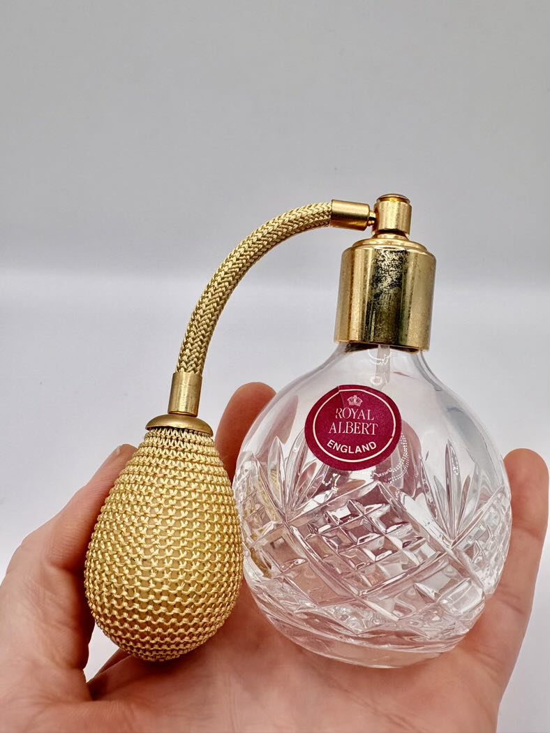 Perfume bottle with gold cap and Royal Albert England label held in hand against a neutral background
