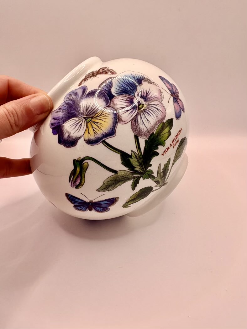 Round container with floral design held by a hand on a light pink background