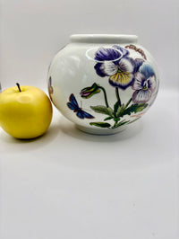 Decorative ceramic jar with floral design next to a yellow apple on a white background