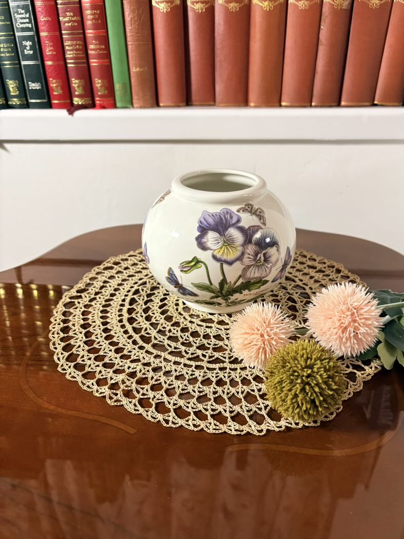 Decorative vase with floral design on a doily with flowers on a wooden surface.