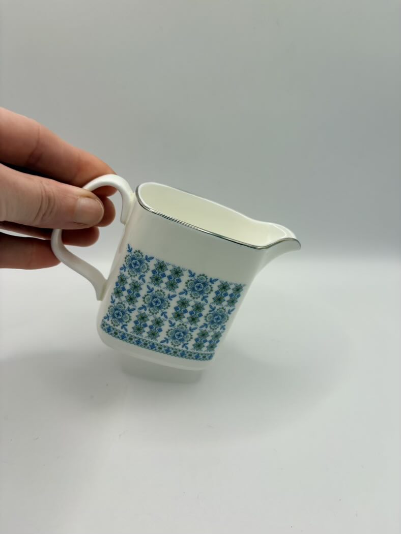 White ceramic pitcher with blue floral pattern held by a hand on a light gray background