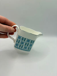 White ceramic pitcher with blue floral pattern held by a hand on a light gray background