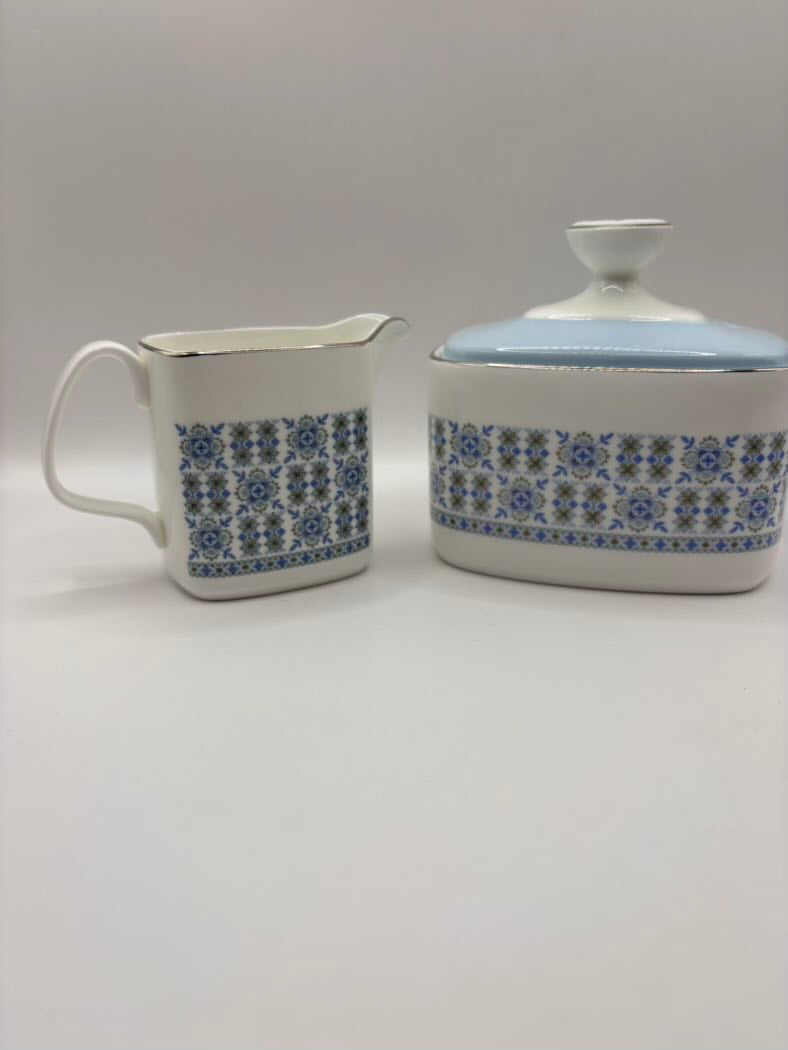 White ceramic creamer and sugar bowl with blue floral pattern on a gray background