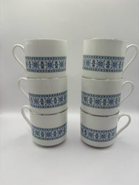 Set of six white mugs with blue floral patterns stacked on a white background