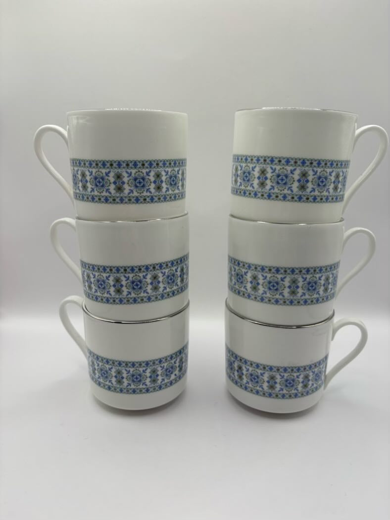 Set of six white mugs with blue floral patterns stacked on a white background
