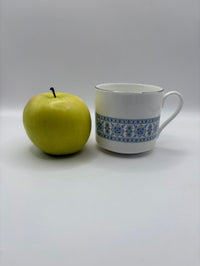 Green apple and white mug with blue patterns on a light gray background
