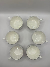 Six white ceramic cups with black rims arranged in a circular pattern on a gray background.
