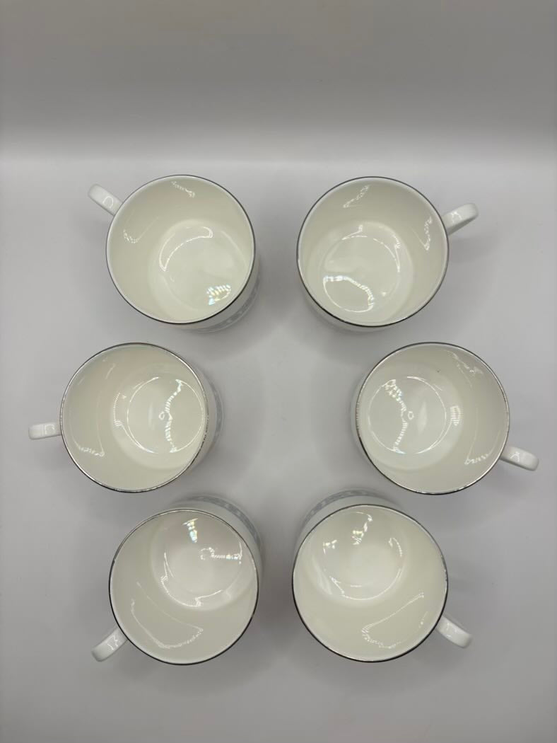 Six white ceramic cups with black rims arranged in a circular pattern on a gray background.