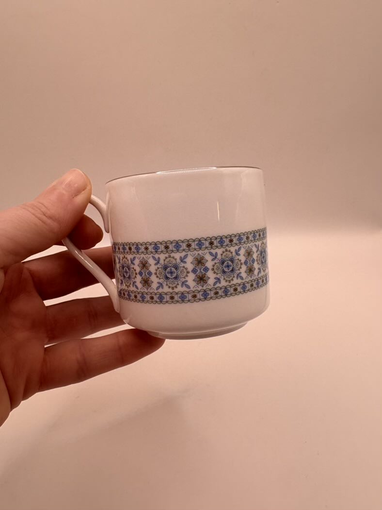 Hand holding a small ceramic cup with decorative band against a plain background