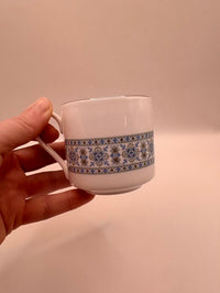 Hand holding a small ceramic cup with decorative band against a plain background
