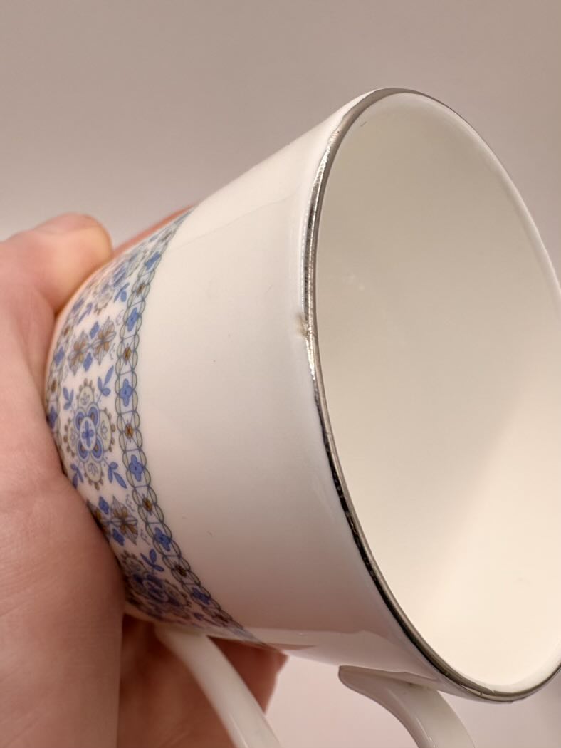 White ceramic cup with floral patterned rim held by a hand against a neutral background