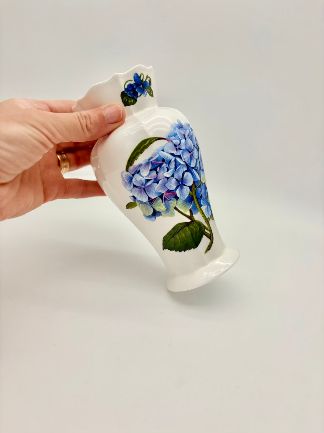 Hand holding a small white ceramic cup with blue floral design on a light gray background