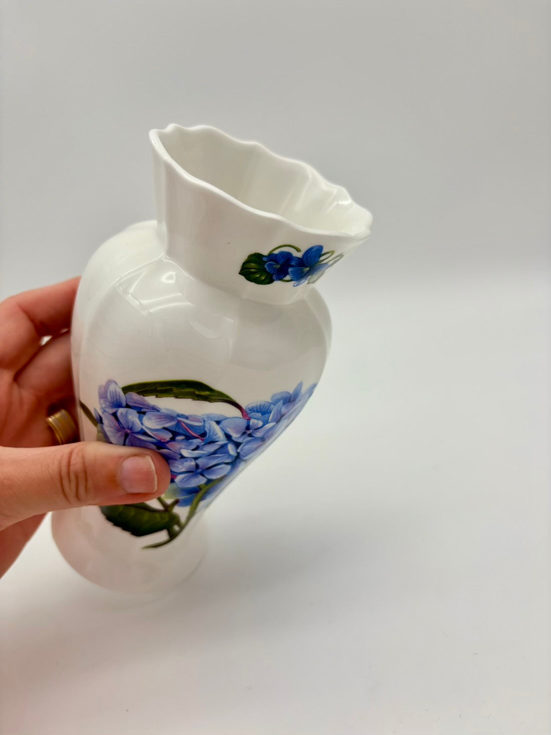 White ceramic pitcher with blue floral design held by a hand on a light gray background