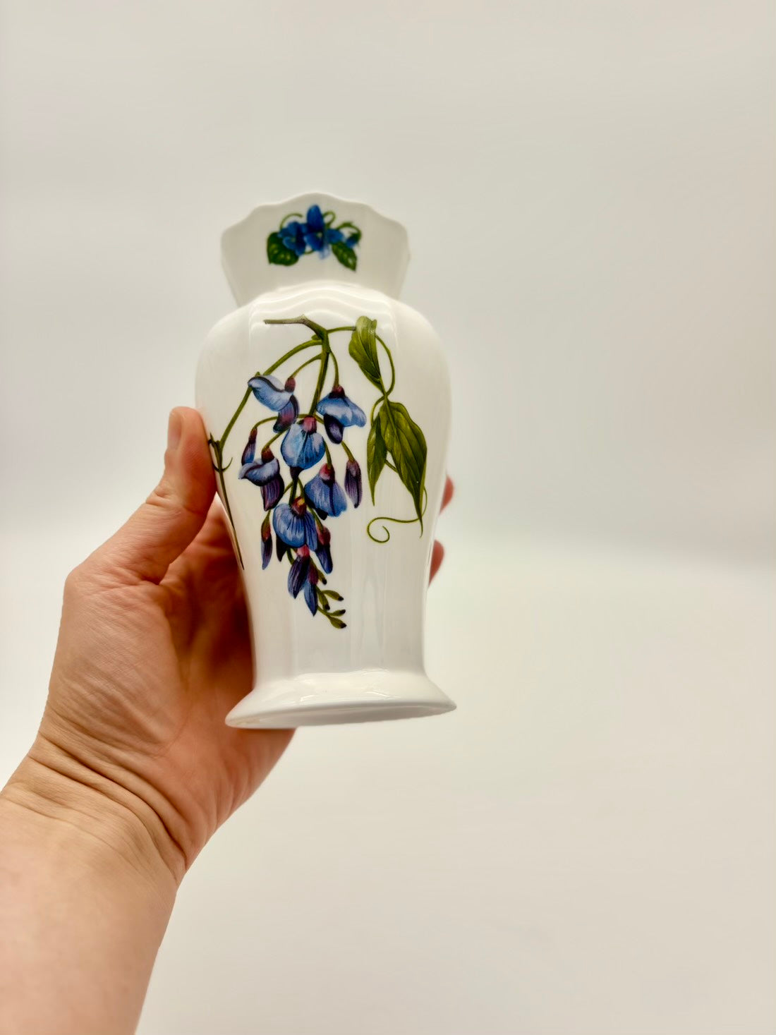 Hand holding a white ceramic jar with floral design on a plain background