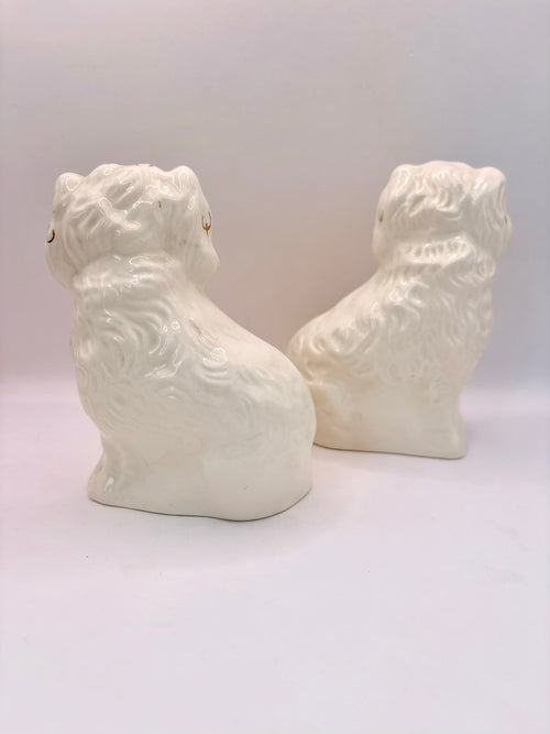 A pair of white ceramic dog figurines with textured fur detailing, shown from the back on a light gray studio background.