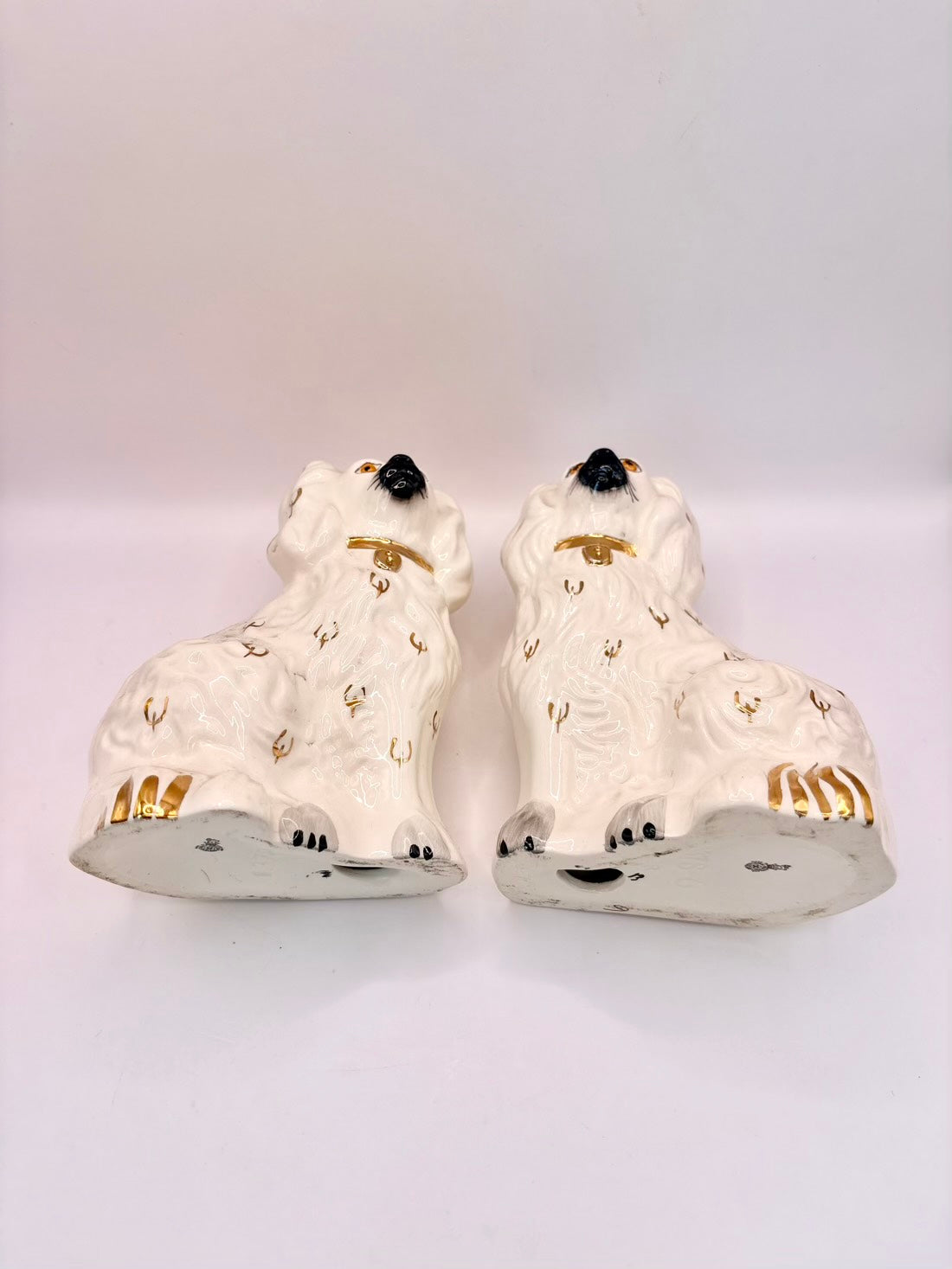 A pair of white ceramic decorative dogs with gold accents, black noses, and black paws, photographed against a plain light background.
