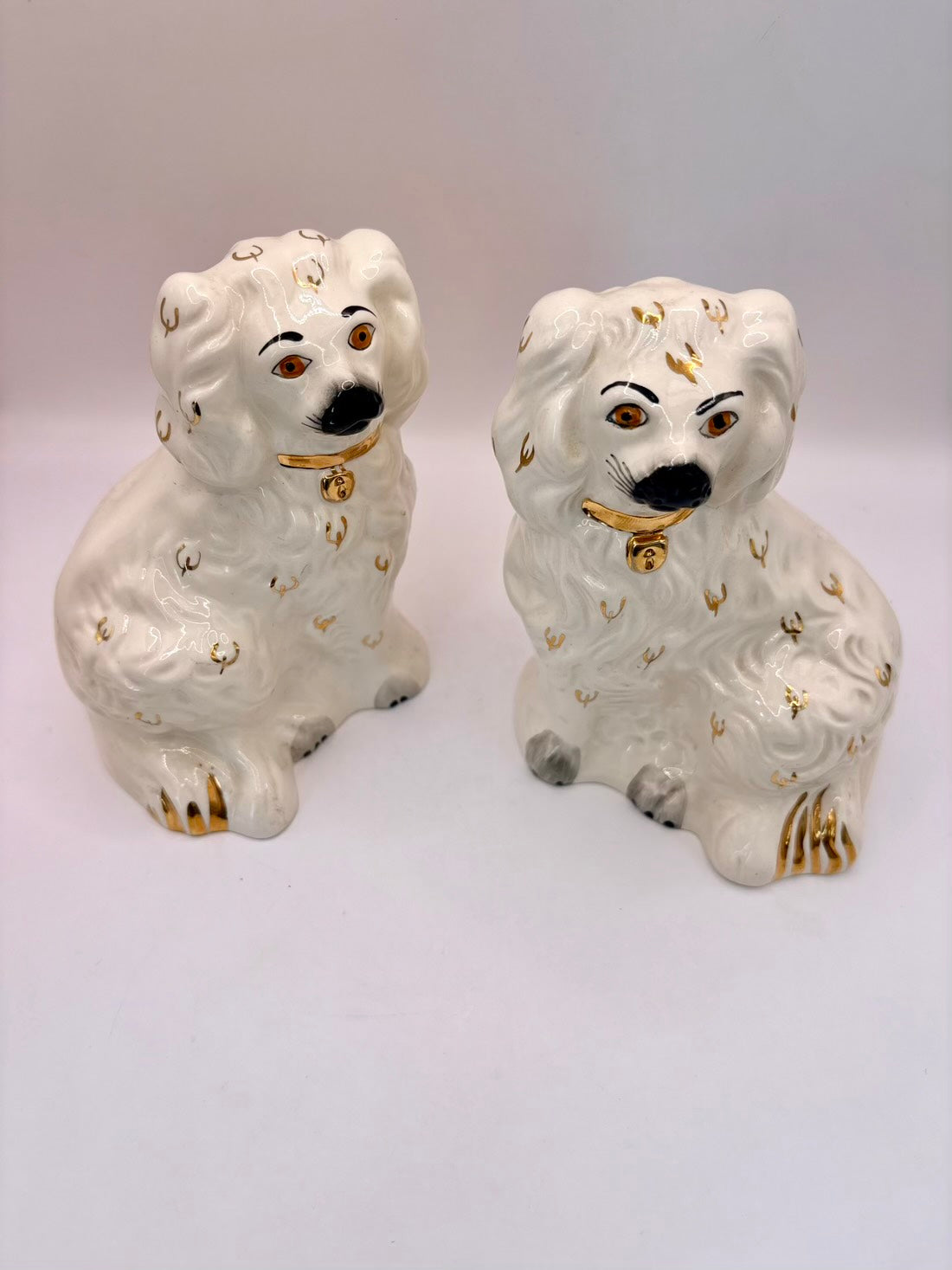 A pair of white ceramic decorative dogs with gold and black painted details, shown on a plain light background.