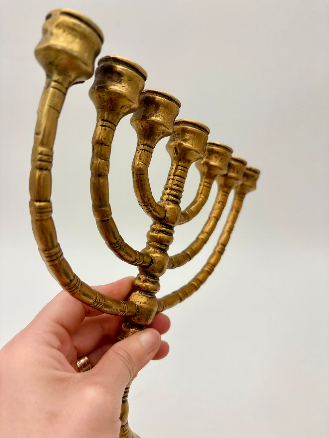 Brass menorah held by a hand against a plain background