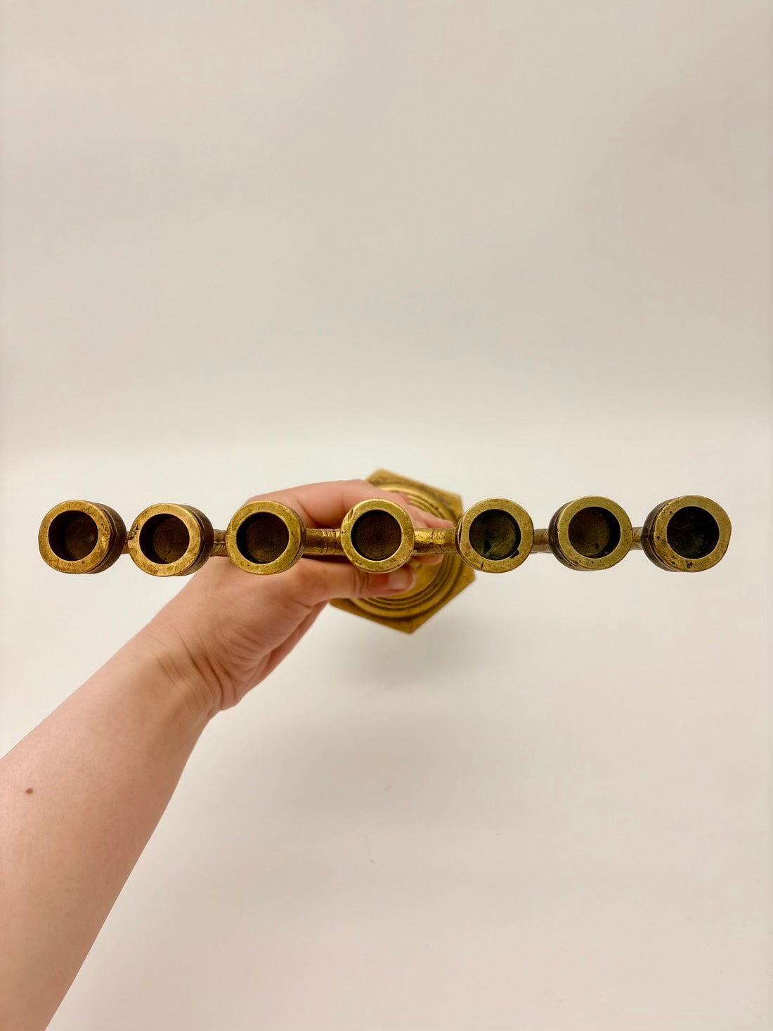 Hand holding a gold candle holder with five cylindrical holders on a plain background
