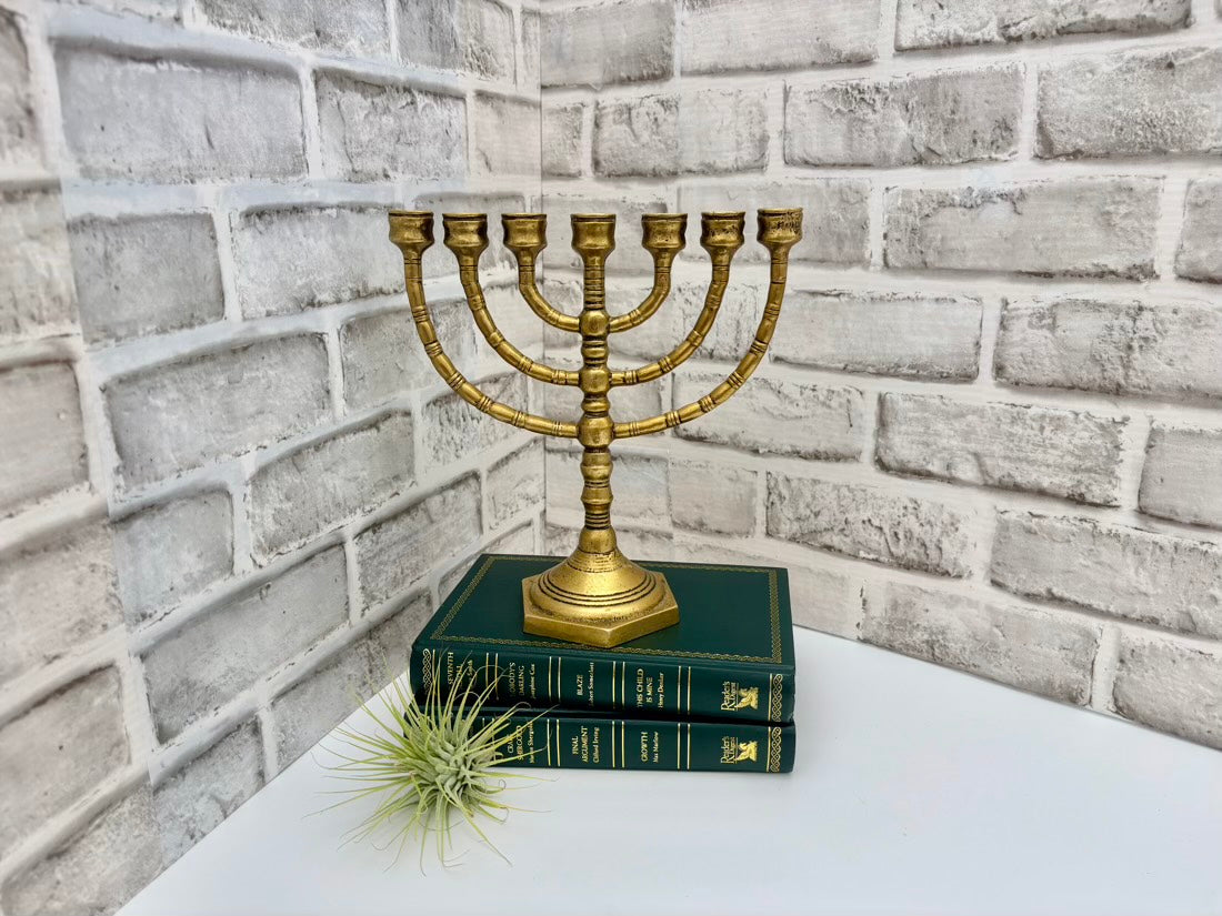 Gold menorah on green books against a brick wall