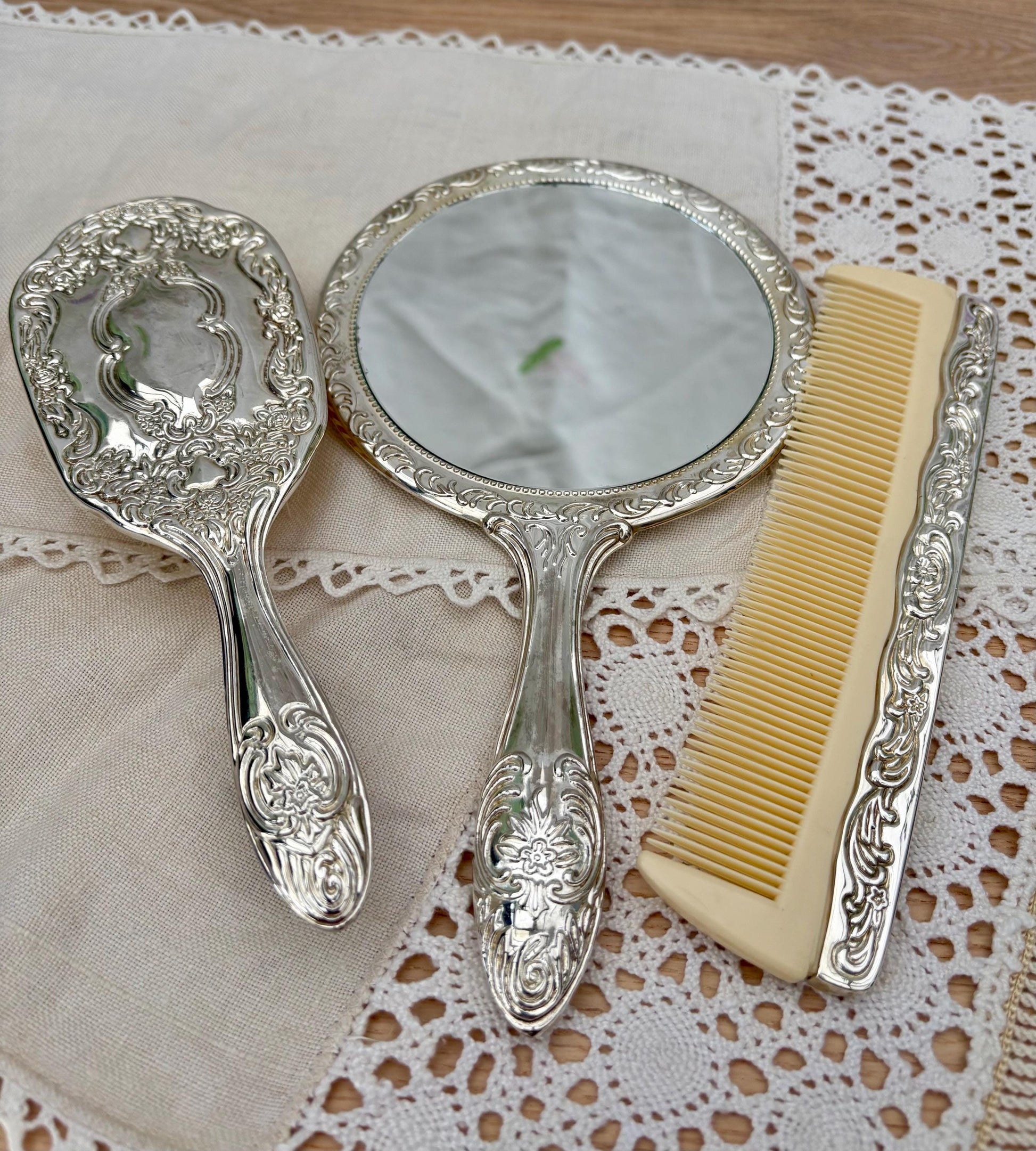 Vintage silver plated vanity set featuring a mirror, brush, and comb with intricate floral designs