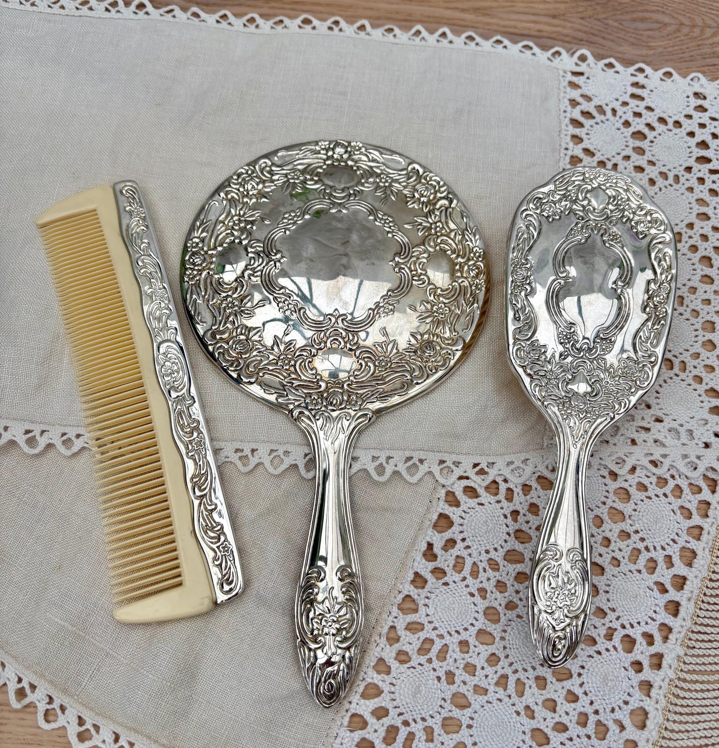 Vintage silver plated vanity set with mirror, brush, and comb featuring intricate floral designs