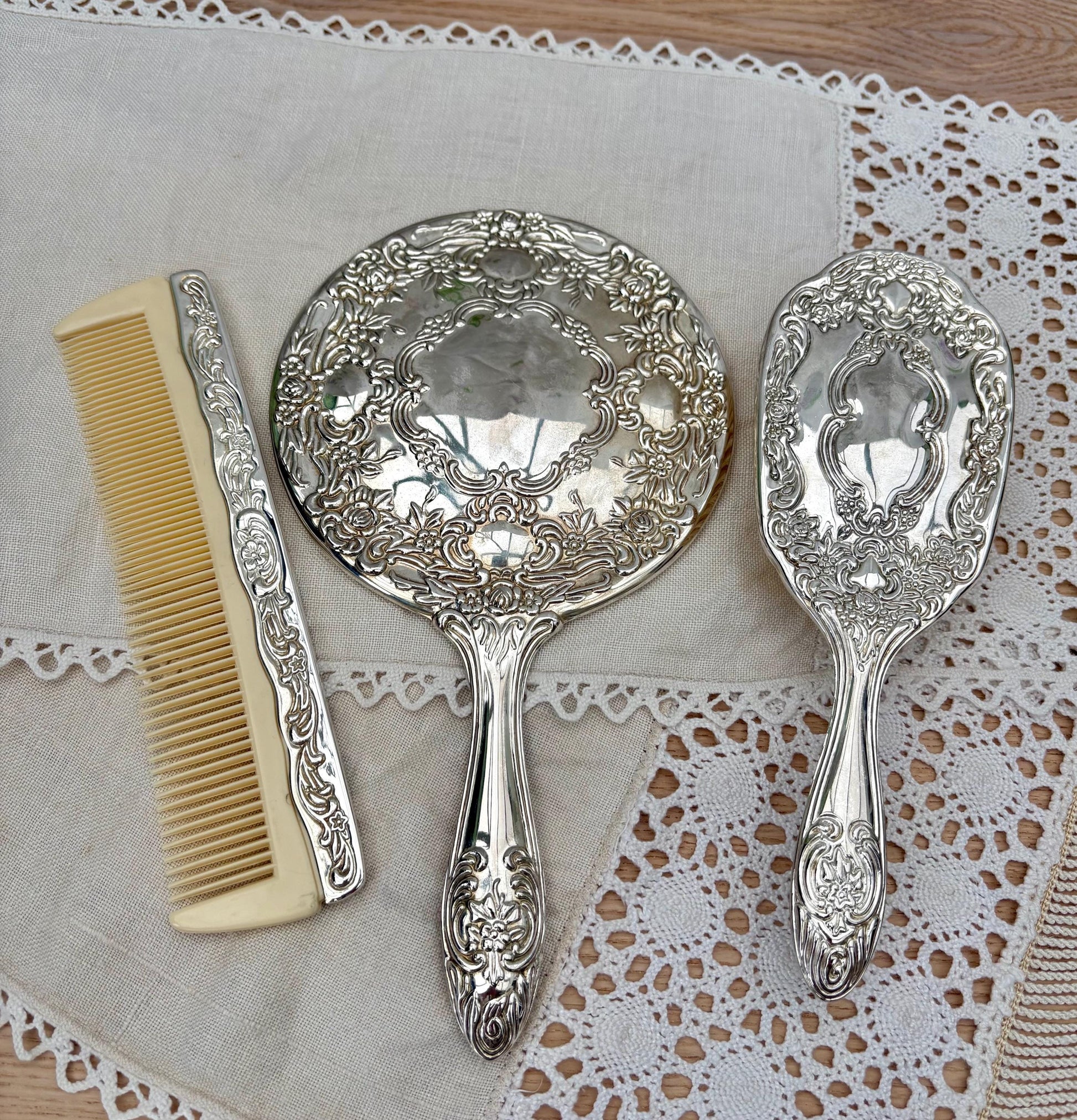 Vintage silver plated vanity set with mirror, brush, and comb featuring intricate floral designs