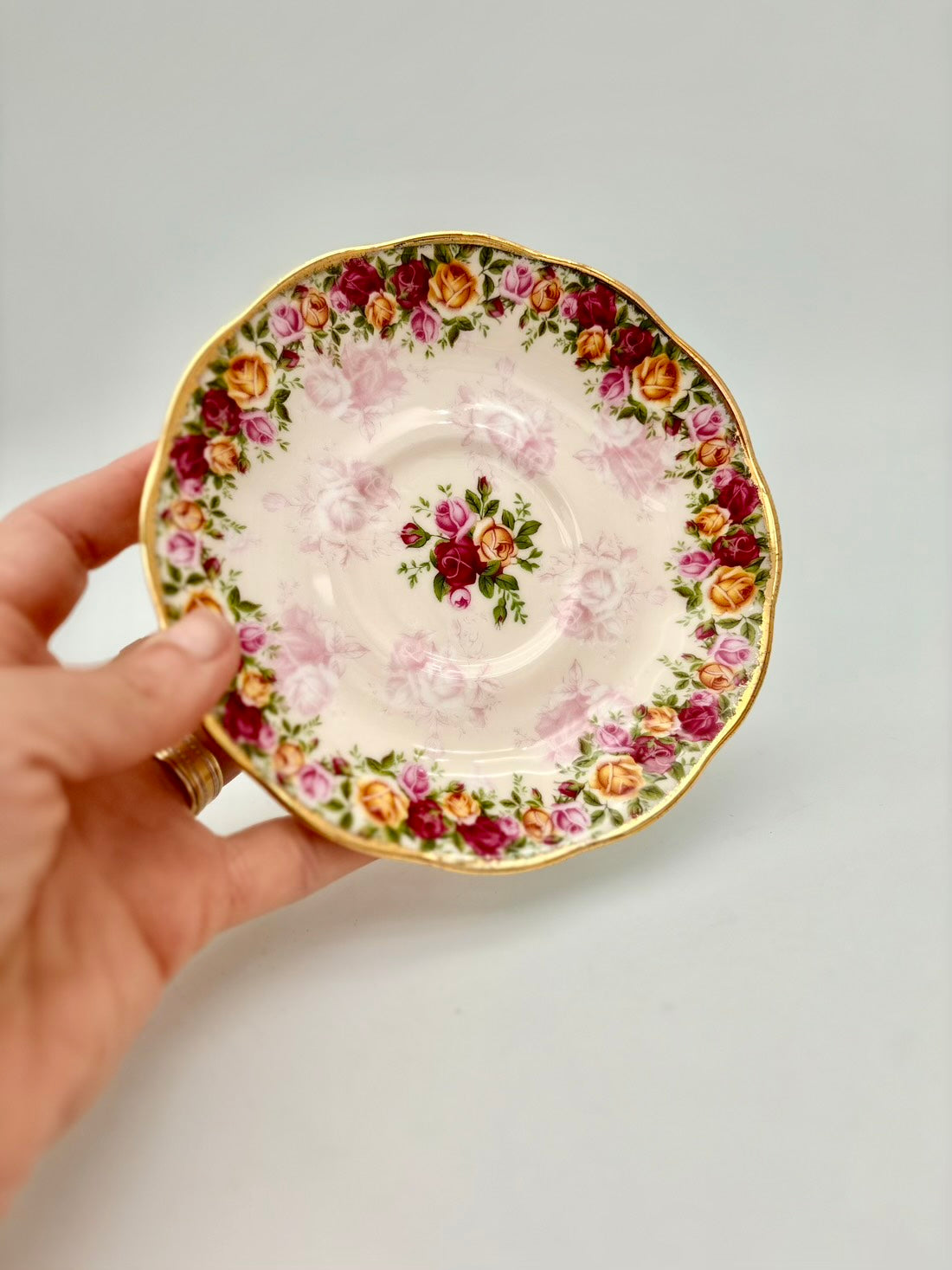 Hand holding a decorative teacup with floral pattern on a plain background