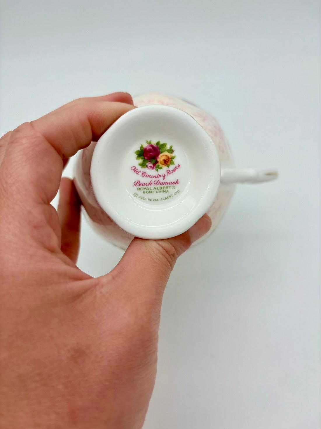 Hand holding a small white container with a decorative label on a light gray background