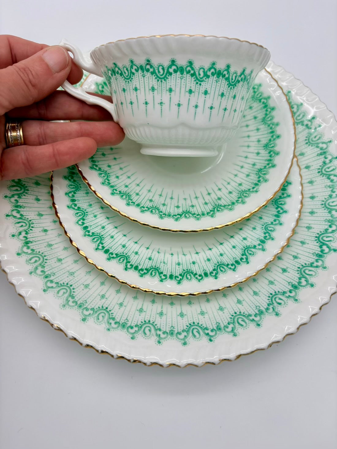 Set of green and white patterned teacup and saucers with a hand holding the cup.