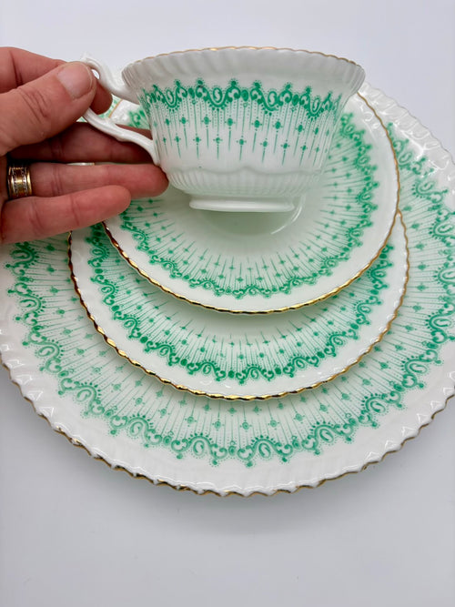Set of green and white patterned teacup and saucers with a hand holding the cup.