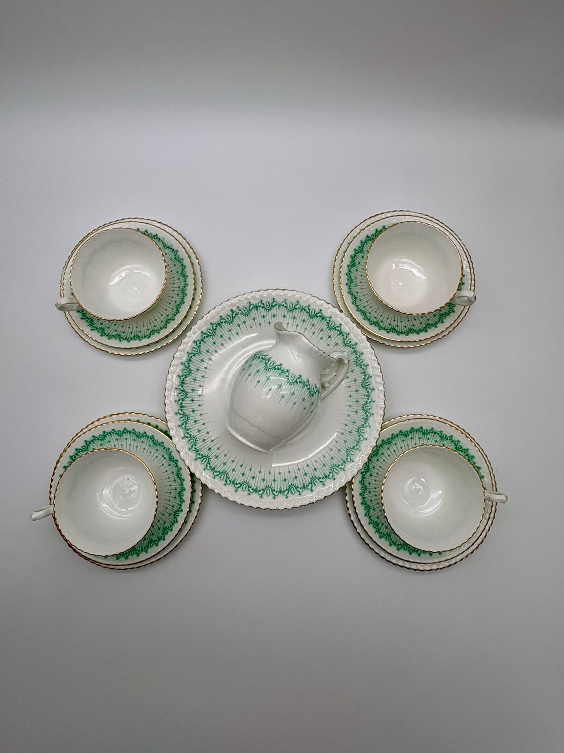Set of ceramic teacups and saucers with green decorative patterns on a gray background