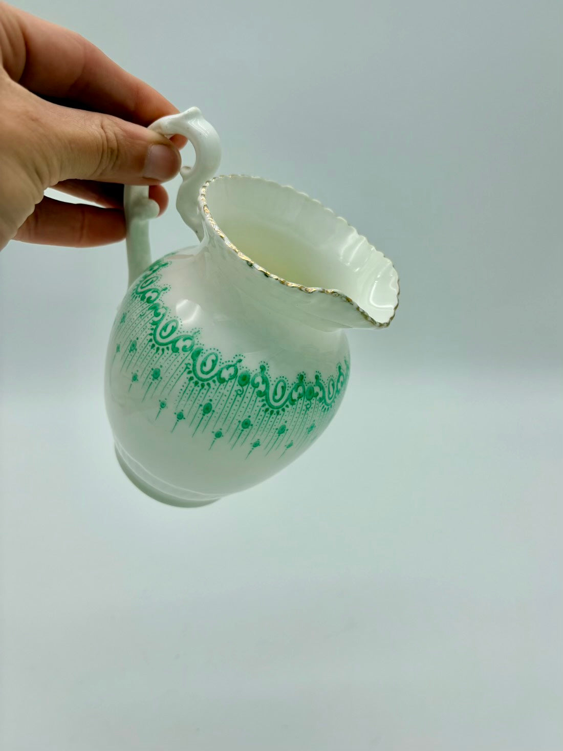White ceramic pitcher with green patterns held by a hand against a light gray background