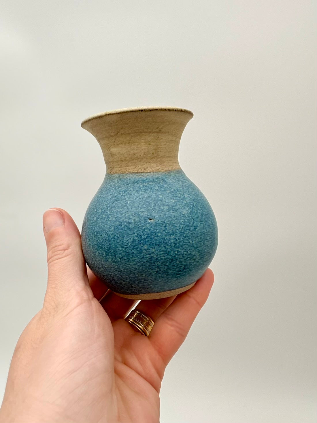 Hand holding a small blue and beige ceramic vase against a plain background