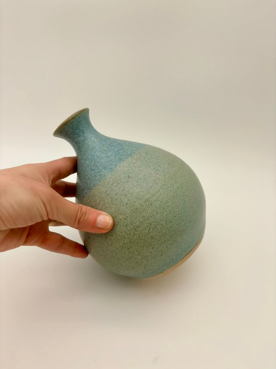 Hand holding a ceramic vase with two-tone design on a plain background